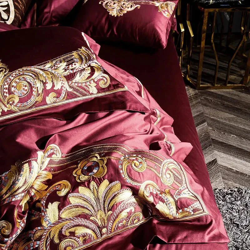 Folded red Egyptian Cotton Sheets with intricate gold and silver thread patterns on a premium bedspread.