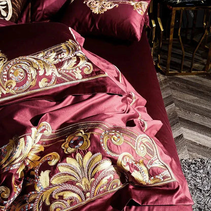 Folded red Egyptian Cotton Sheets with intricate gold and silver thread patterns on a premium bedspread.